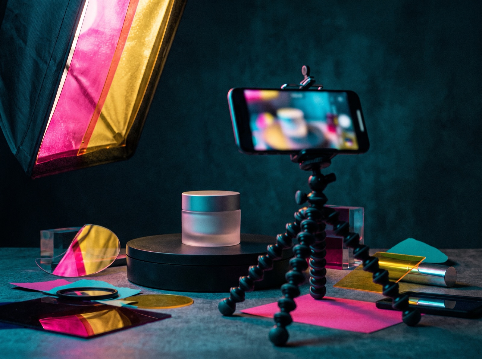 A phone on a small tripod filming a cosmetics jar in studio light